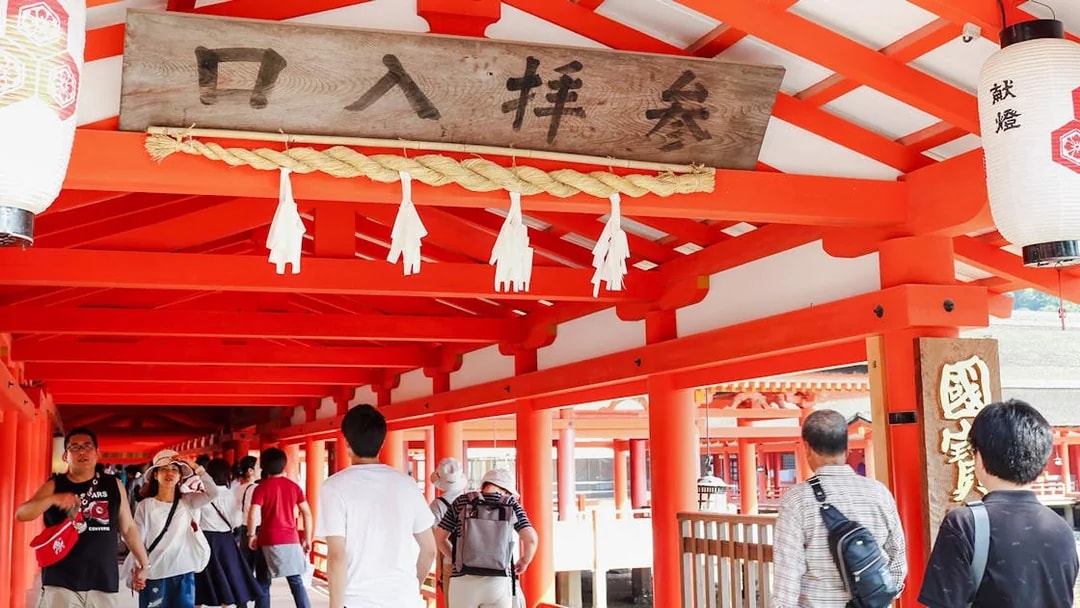 Visitors walking through the vibrant red corridors of Itsukushima Shrine, Japan.