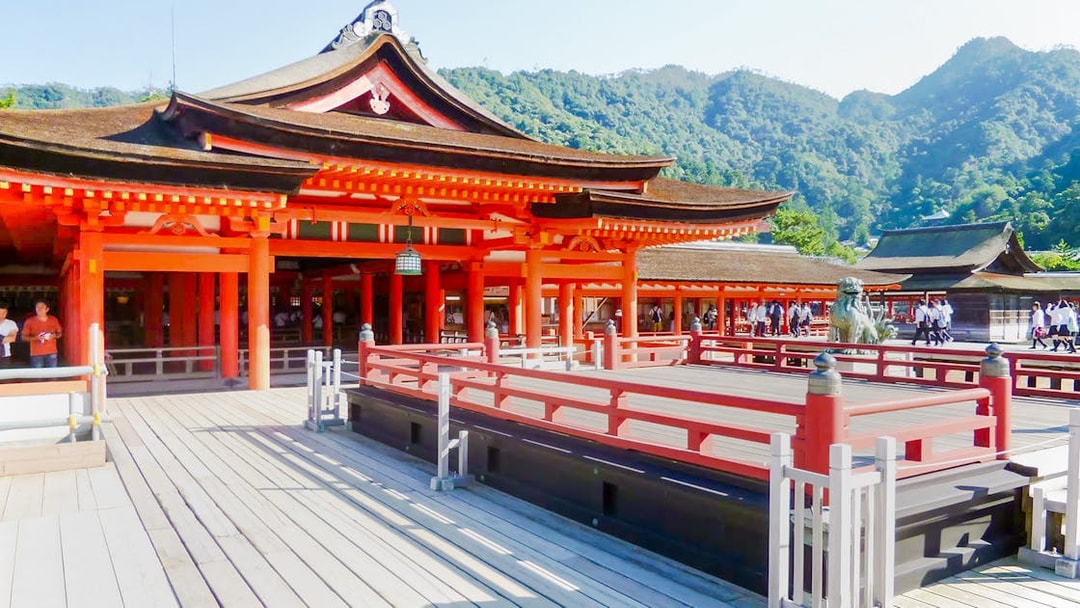 Itsukushima Shrine with red wooden structures and mountainous backdrop in Japan.