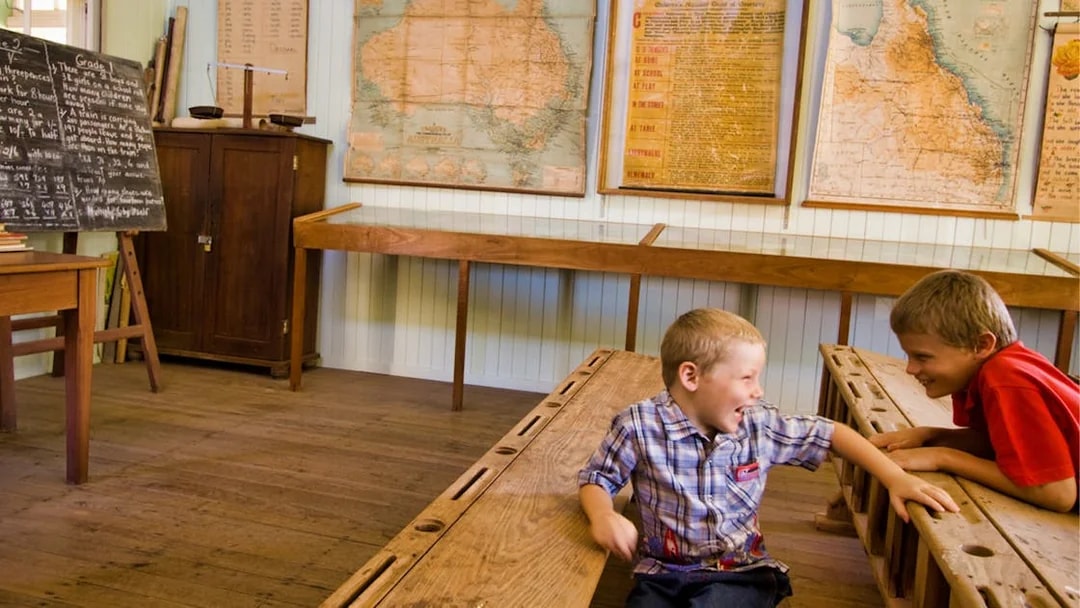 Children in a historic classroom at Herberton Historic Village, Australia, with vintage maps and chalkboard.