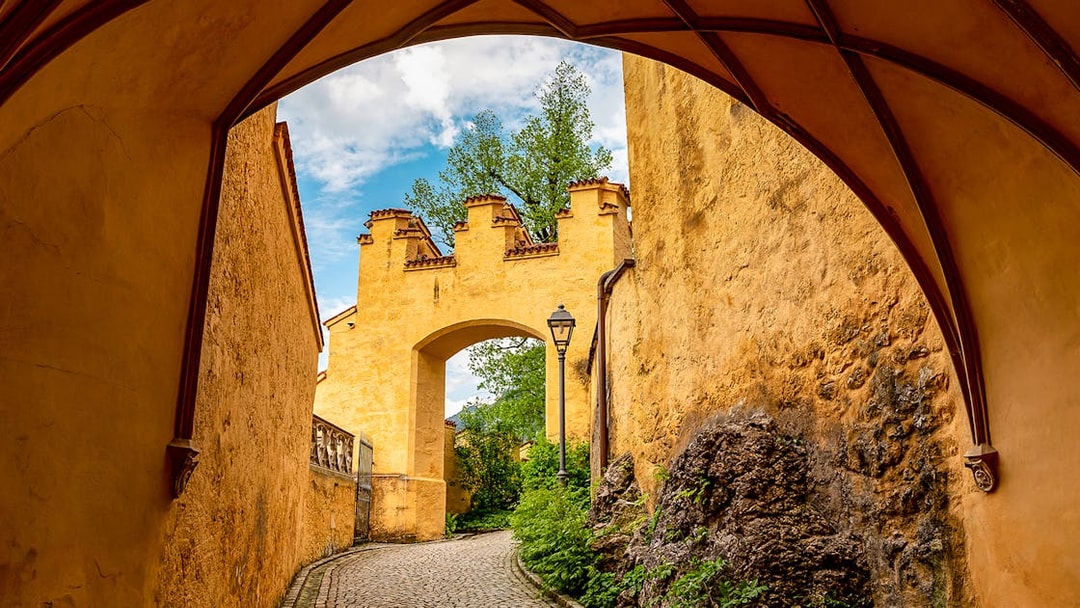 Hohenschwangau Castle archway with cobblestone path and greenery.