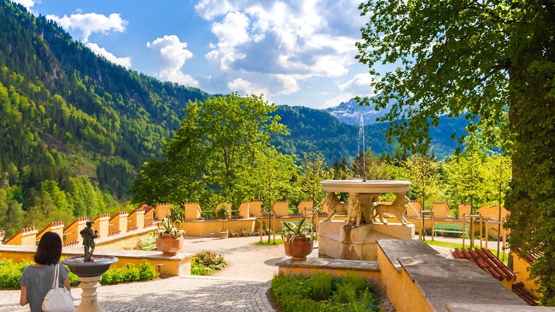 Visitor exploring Hohenschwangau Castle garden with mountain view.