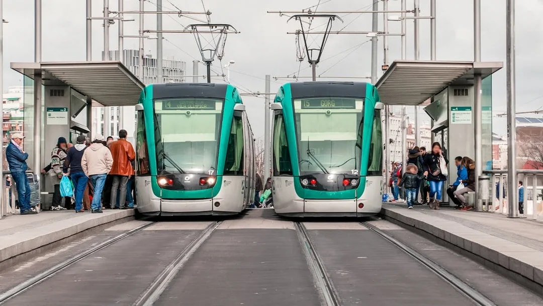 Tourists boarding trams at a Barcelona station with cityscape views.