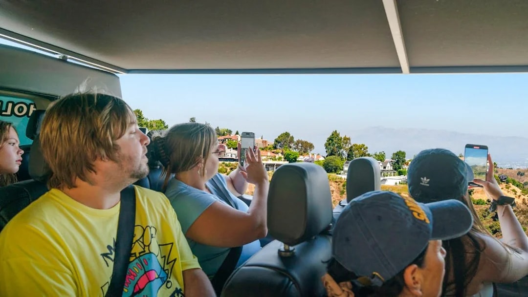Tourists on Hollywood Sightseeing bus capturing views of celebrity homes, Los Angeles.
