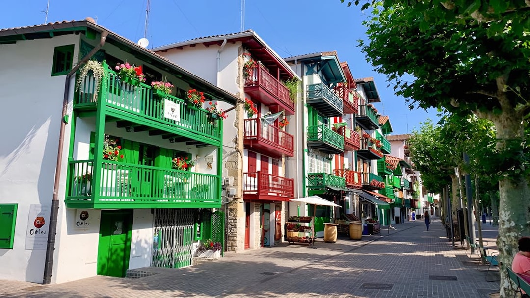 Colorful buildings with balconies in Hondarribia, Spain, on a sunny street lined with trees.