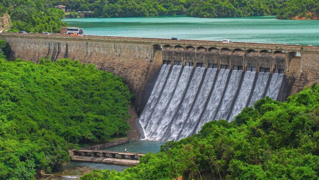 Big Bus tour passing over a dam with cascading water and lush greenery.