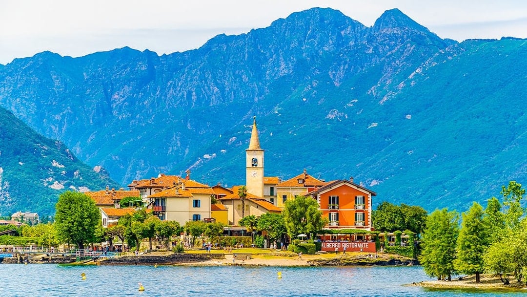 Island village with church tower and colorful buildings on Isole Borromee, Italy, viewed from the water.