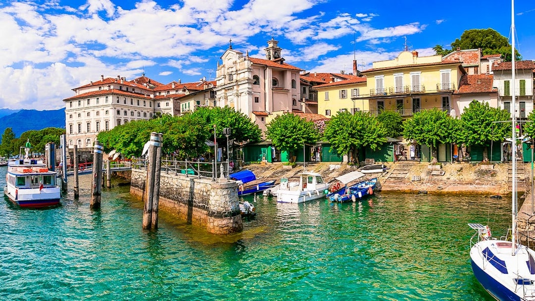 Hop-on hop-off boat docked at Isole Borromee with historic buildings in the background.