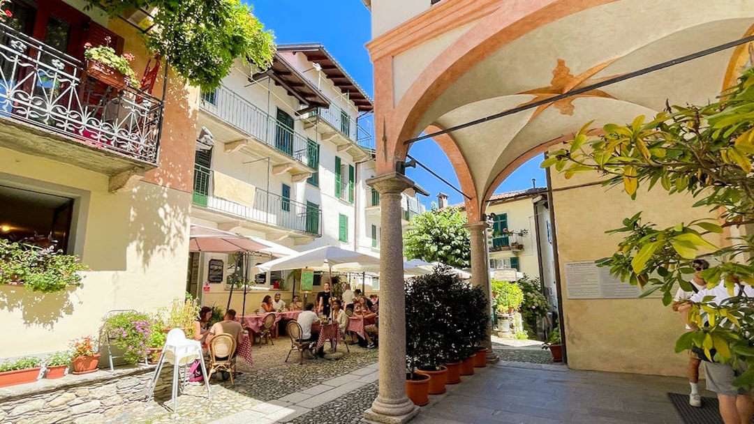 Outdoor café scene on Isole Borromee with people dining under umbrellas, surrounded by historic architecture.