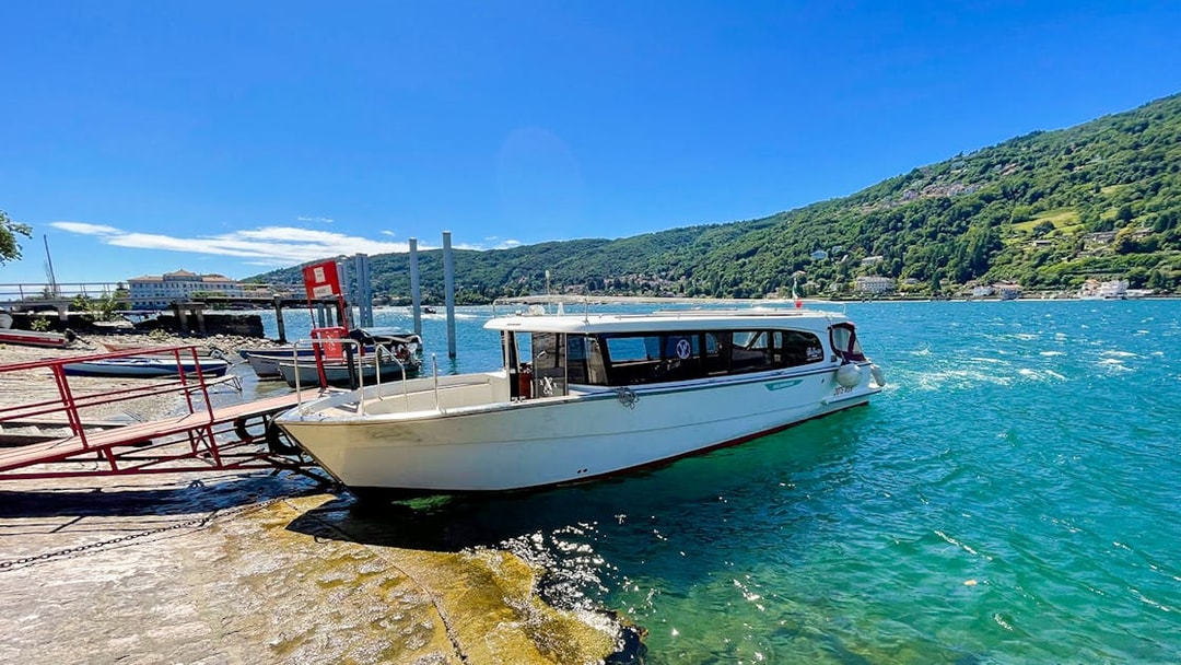 Boat docked at Isole Borromee for Hop-on Hop-off tour, with scenic lake and hills in background.