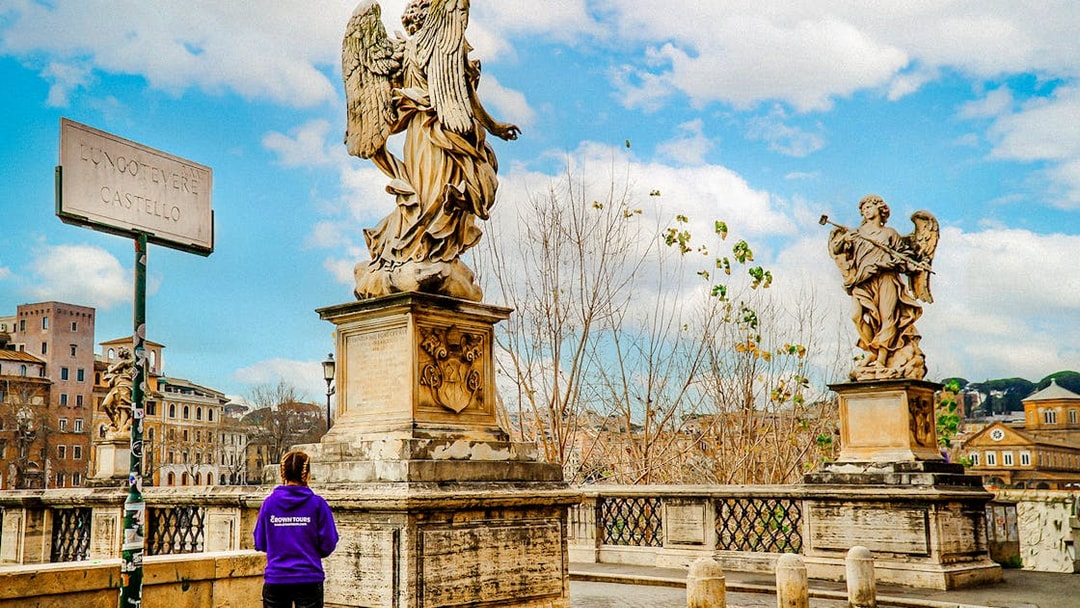 Statues on Ponte Sant'Angelo near Castel Sant'Angelo, Rome, with a tour guide in view.