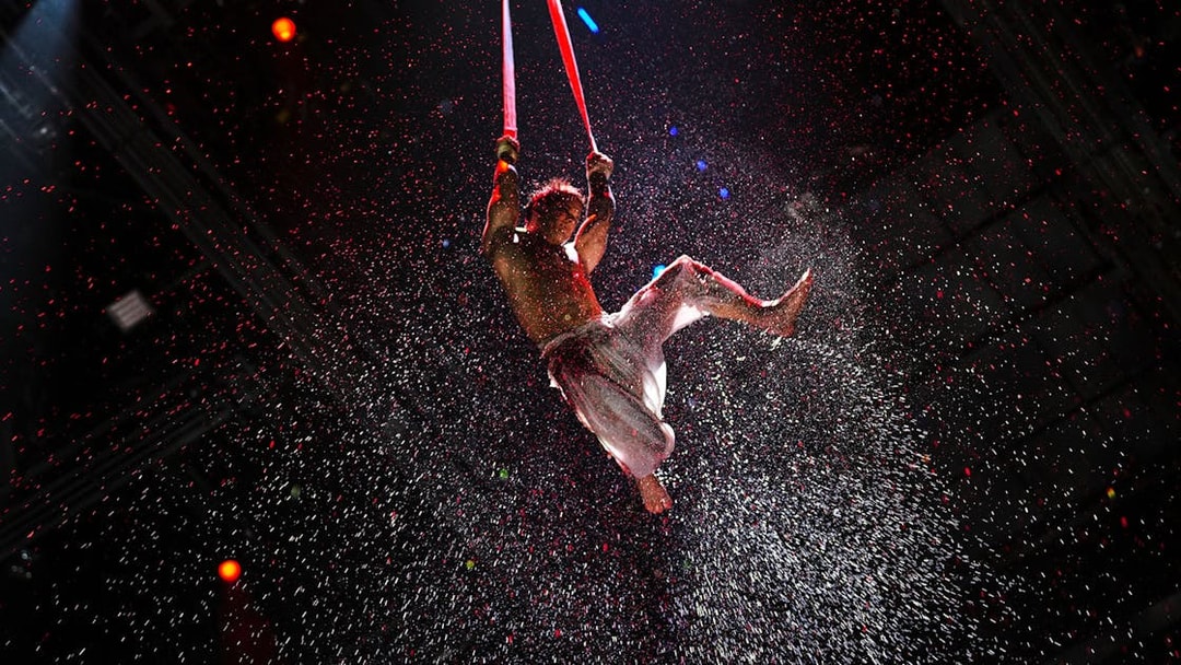 Aerial performer suspended in water spray during House of Dancing Water show.