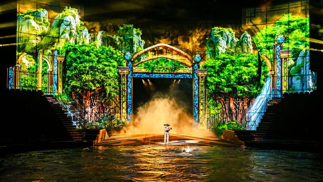 Performer on stage with water and lush forest backdrop during House of Dancing Water show.