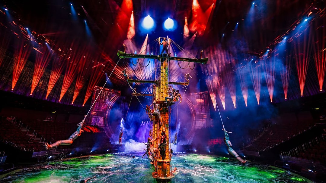 Performers on a ship mast during House of Dancing Water show with vibrant lights.