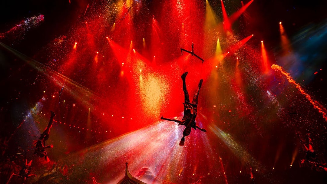 Acrobat performing mid-air during House of Dancing Water show with vibrant red lighting.