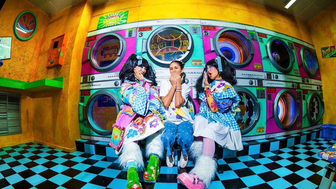Colorful laundromat scene with three people in playful costumes, part of House of Hype experience.