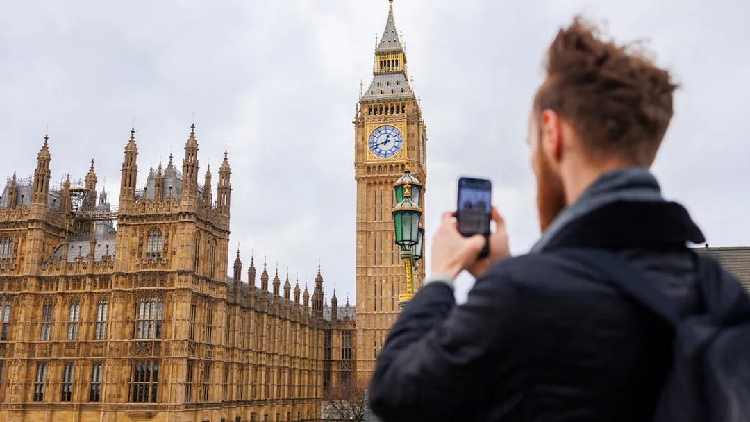 Visitor photographing Big Ben and Houses of Parliament, London.