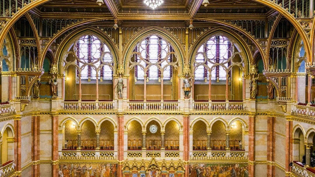 Interior of the House of Peers, Hungarian Parliament, Budapest, showcasing ornate arches and stained glass windows.