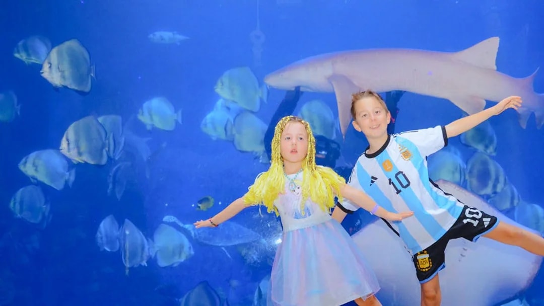 Children posing in front of a large aquarium tank at Hurghada Grand Aquarium.