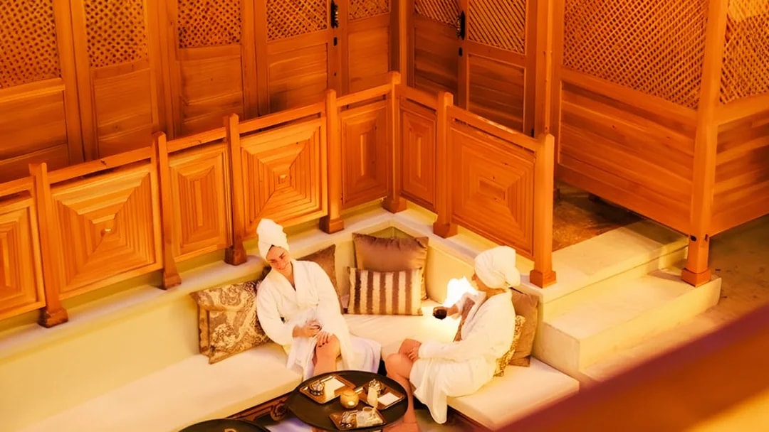 Two people relaxing in Hurrem Sultan Hamam, Istanbul, with wooden decor and cushions.