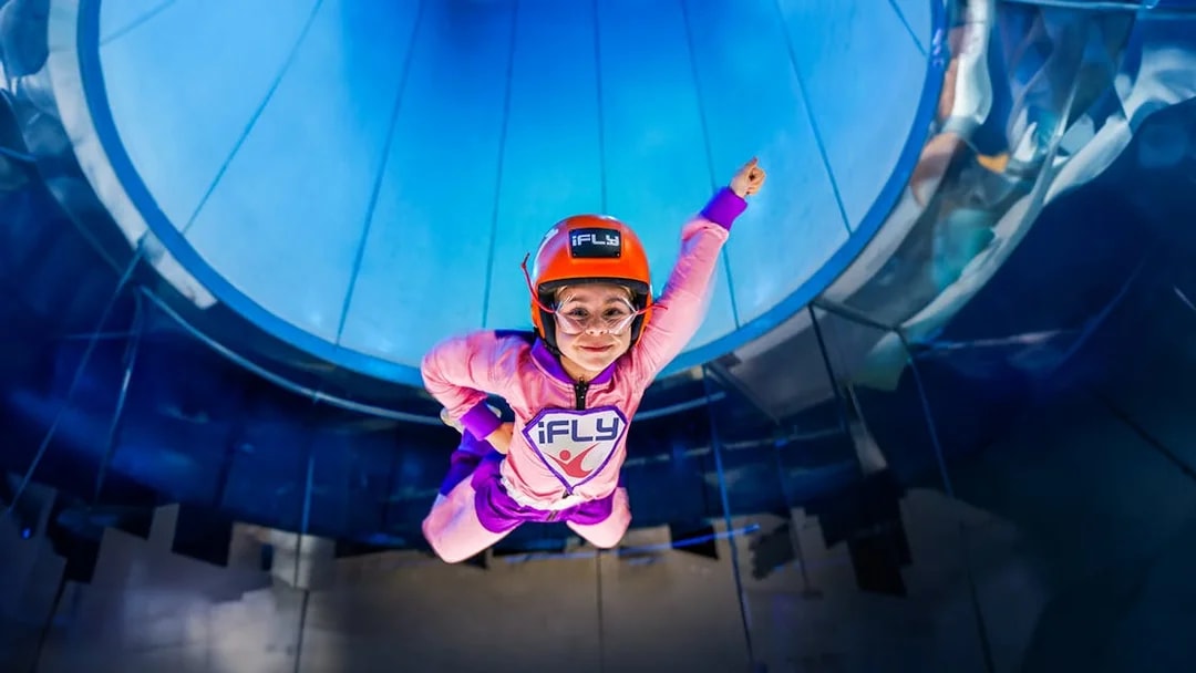 Child enjoying iFLY indoor skydiving experience in a wind tunnel.