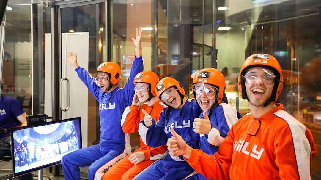 Group of people in flight suits and helmets excited for iFLY Indoor Skydiving Experience.