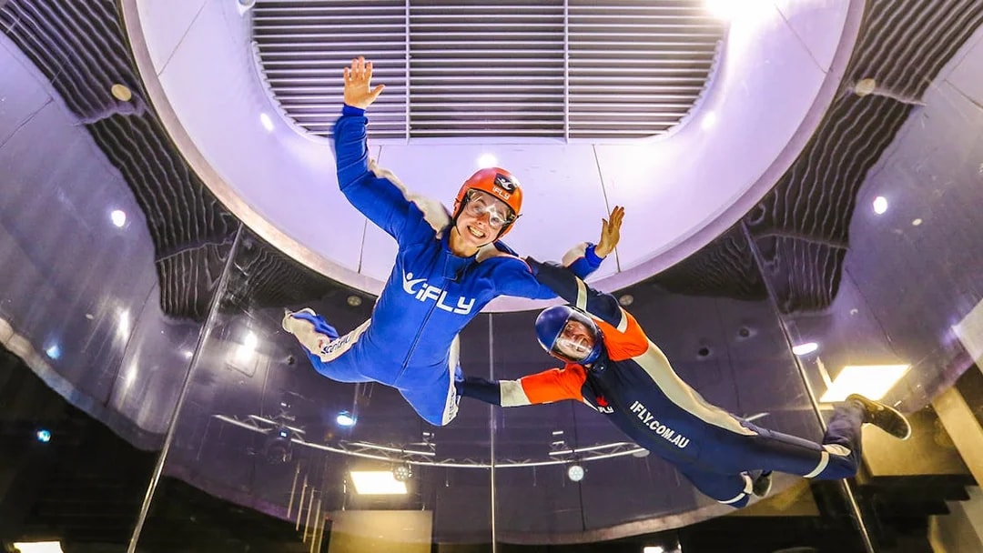 Indoor skydiving at iFLY with instructor guiding participant in wind tunnel.