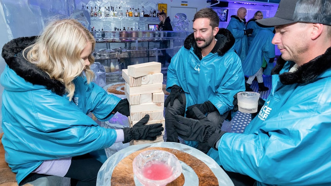 Guests playing Jenga at IceBar Surfers Paradise, wearing blue parkas and holding drinks.