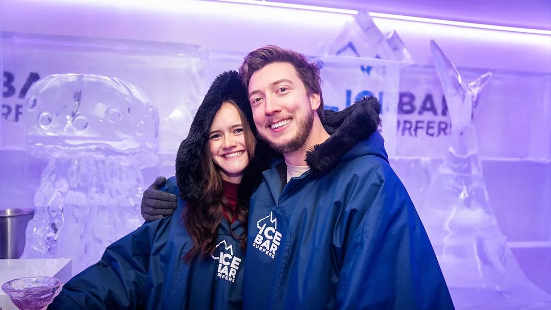Couple in blue parkas enjoying IceBar Surfers Paradise with ice sculptures in the background.