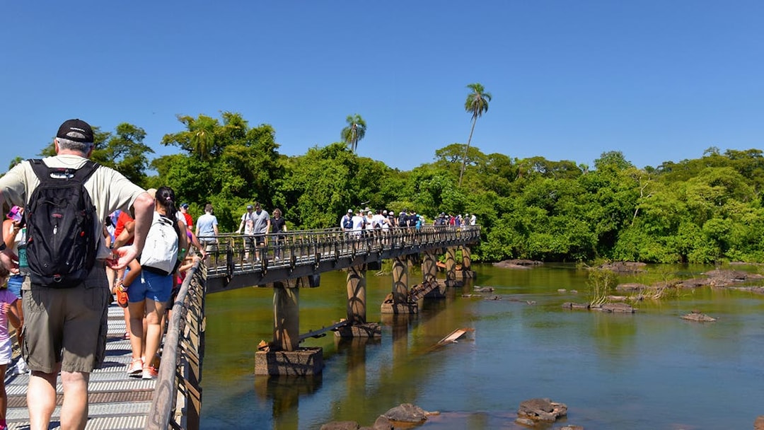 Visitors walking on a bridge towards Iguazu Falls, surrounded by lush greenery.