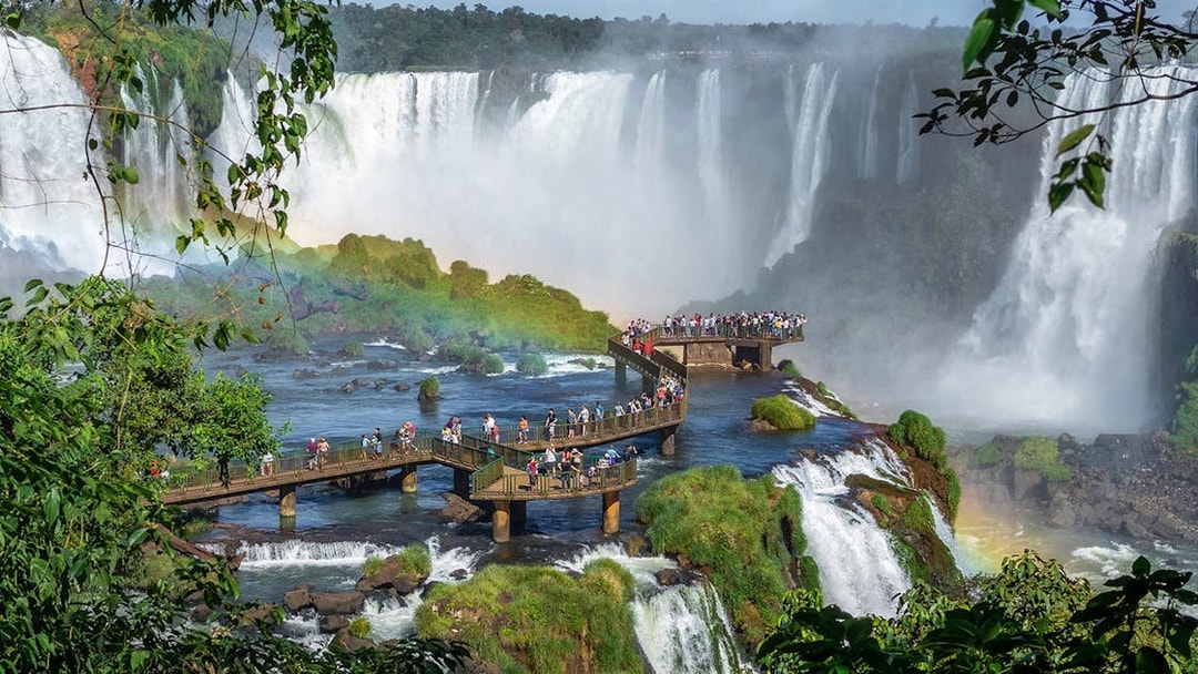 Tourists on a walkway at Iguazu Falls, surrounded by lush greenery and cascading water.