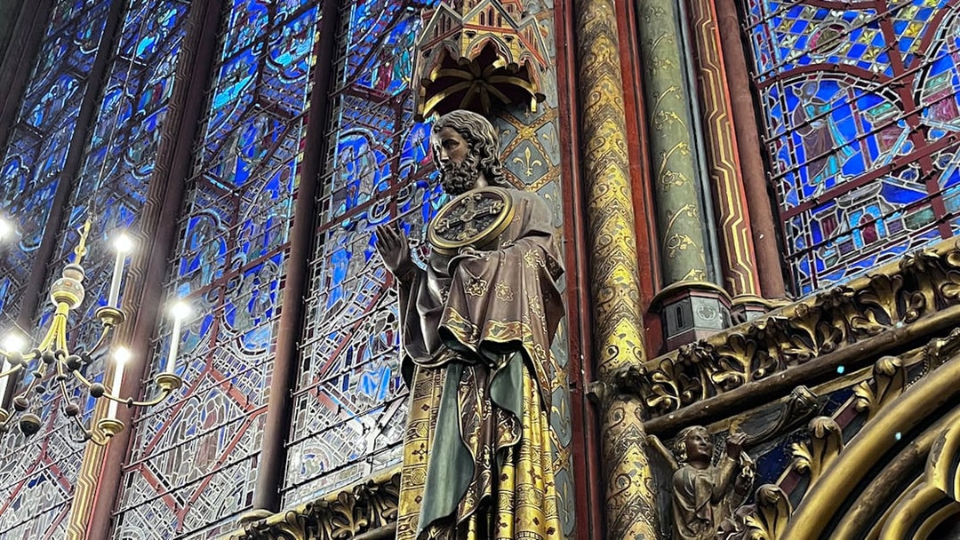 Statue inside Sainte Chapelle with intricate stained glass backdrop, Paris.