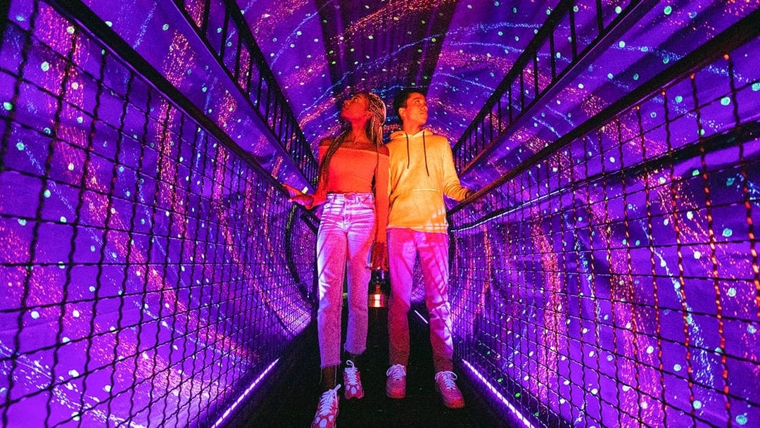 Visitors exploring a vibrant light tunnel at Illuseum Berlin.