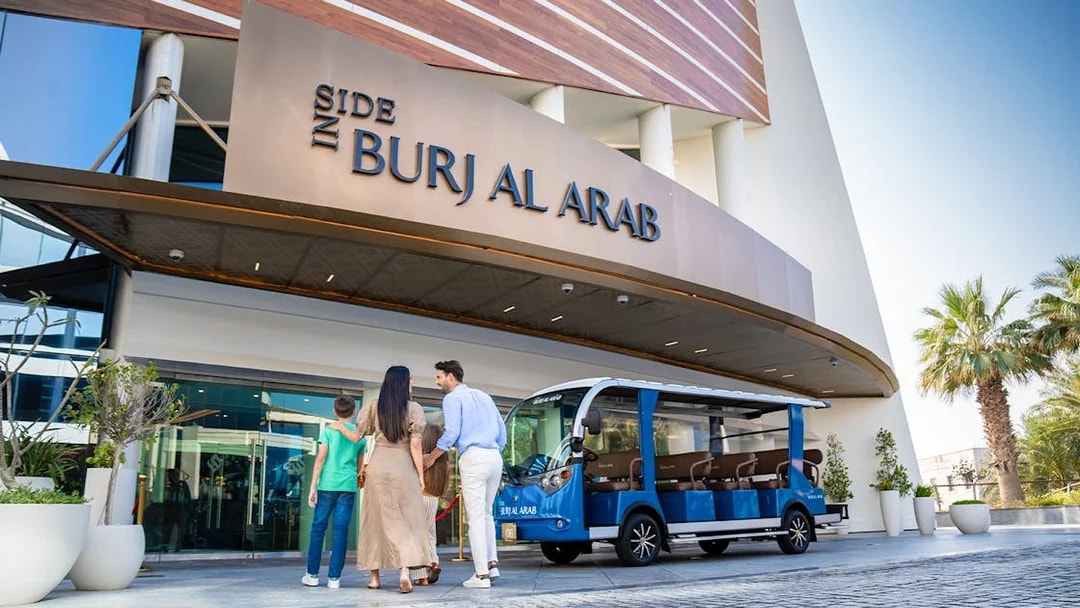 Family entering Burj Al Arab with tour vehicle parked outside.