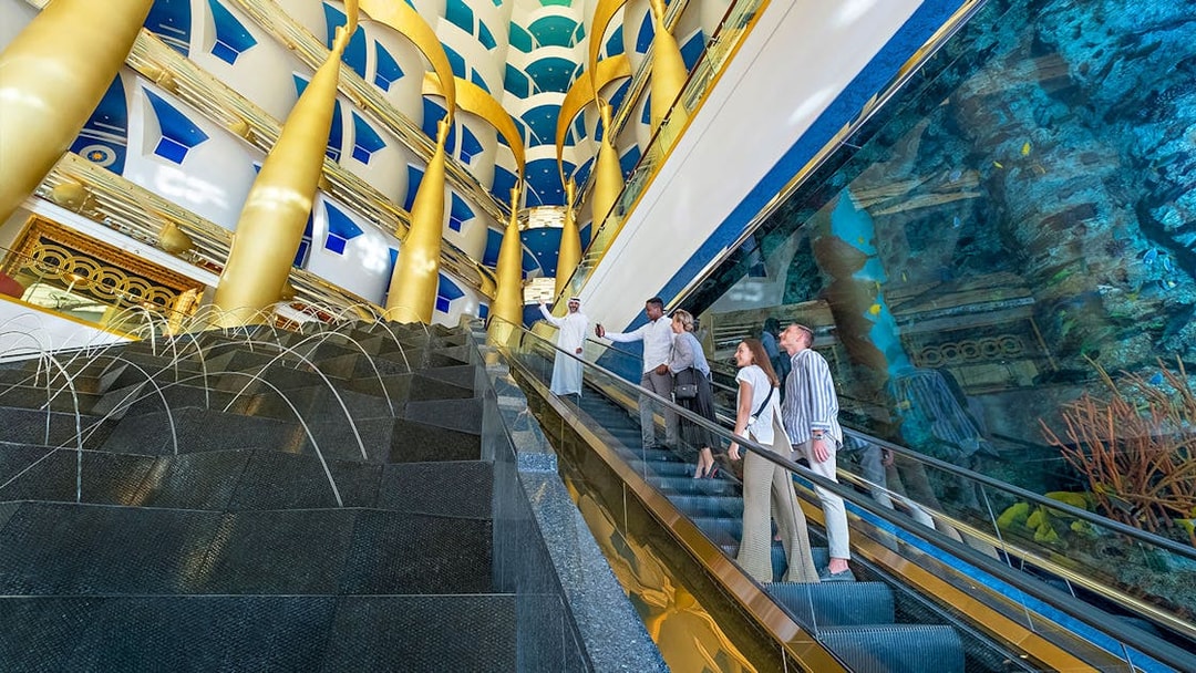 Guests on escalator inside Burj Al Arab, Dubai, with gold columns and aquarium view.