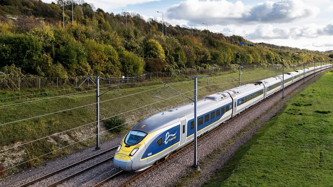 Eurostar train traveling through countryside with green hills and cloudy sky.