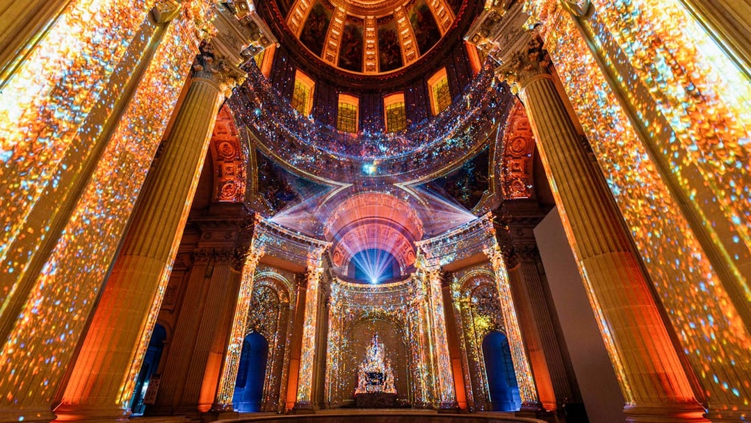 Immersive light display inside Invalides, Paris, showcasing vibrant projections on columns and ceiling.