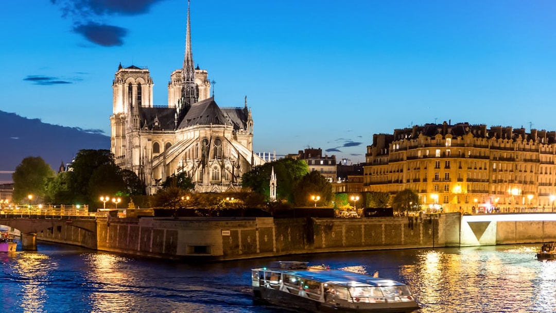 Seine River cruise boat passing Notre-Dame Cathedral at dusk in Paris.