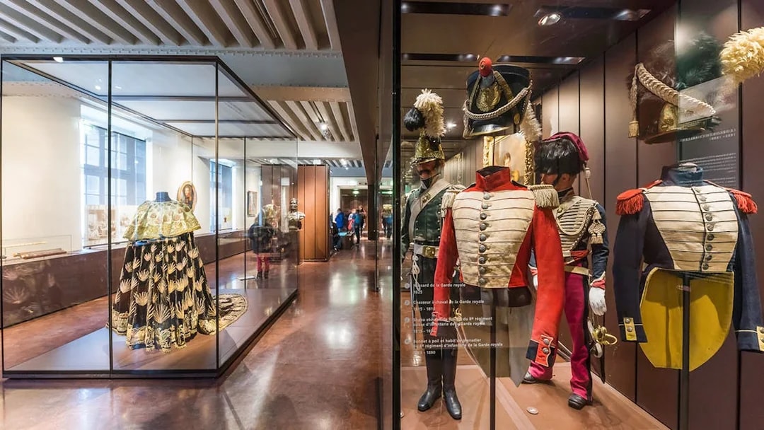 Armour suits and uniforms displayed at Army Museum, Paris with visitors exploring exhibits.