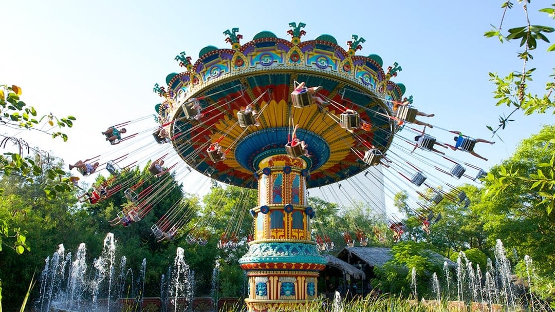 Swing ride at Isla Magica's The Flight of the Falcon, surrounded by trees and fountains.