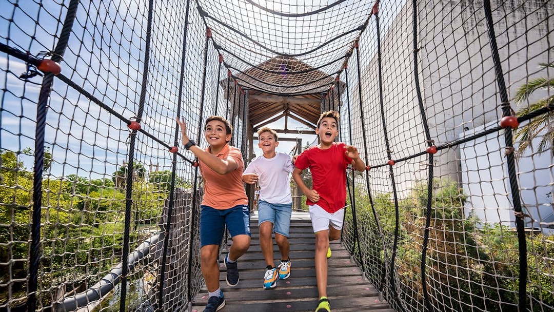 Children running on a rope bridge at Isla Mágica adventure park.