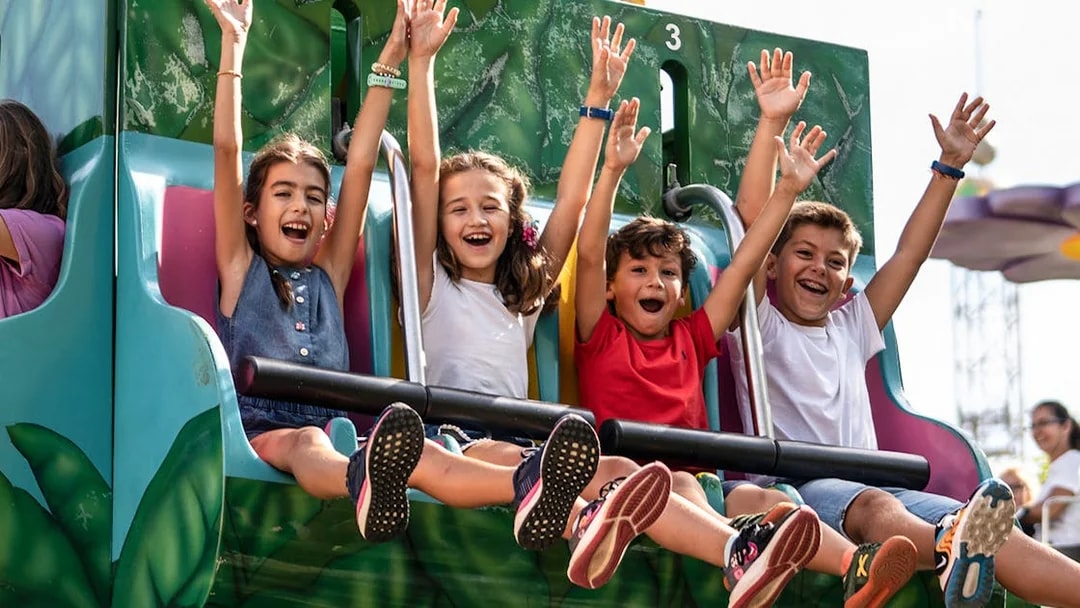 Children enjoying a ride at Isla Mágica, Seville, with arms raised in excitement.
