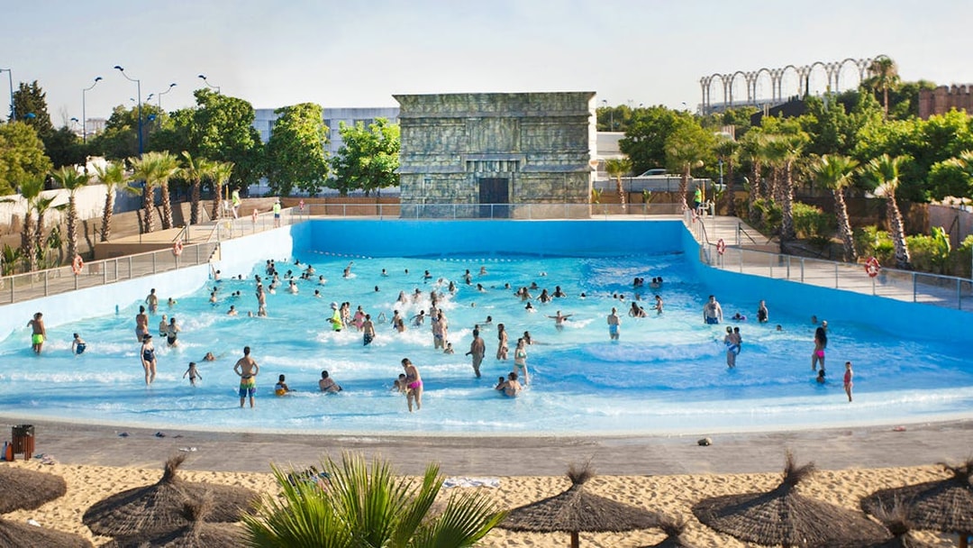 Visitors enjoying the wave pool at Isla Mágica, surrounded by palm trees and a sandy beach.