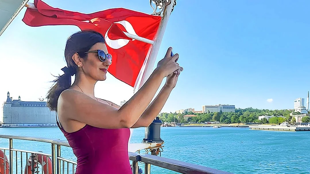 Woman taking photo on ferry with Turkish flag, Istanbul Asian Side in background.