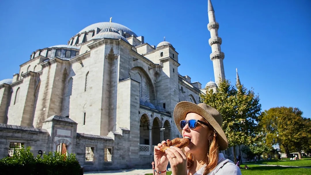 Visitor enjoying simit in front of a mosque during a walking tour in Istanbul.