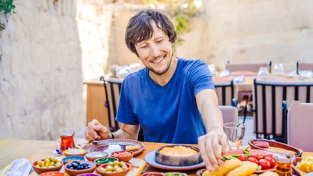 Man enjoying Turkish breakfast with various dishes and tea.