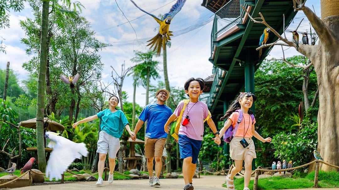 Children enjoying a walk at Jakarta Bird Land with colorful parrots flying above.