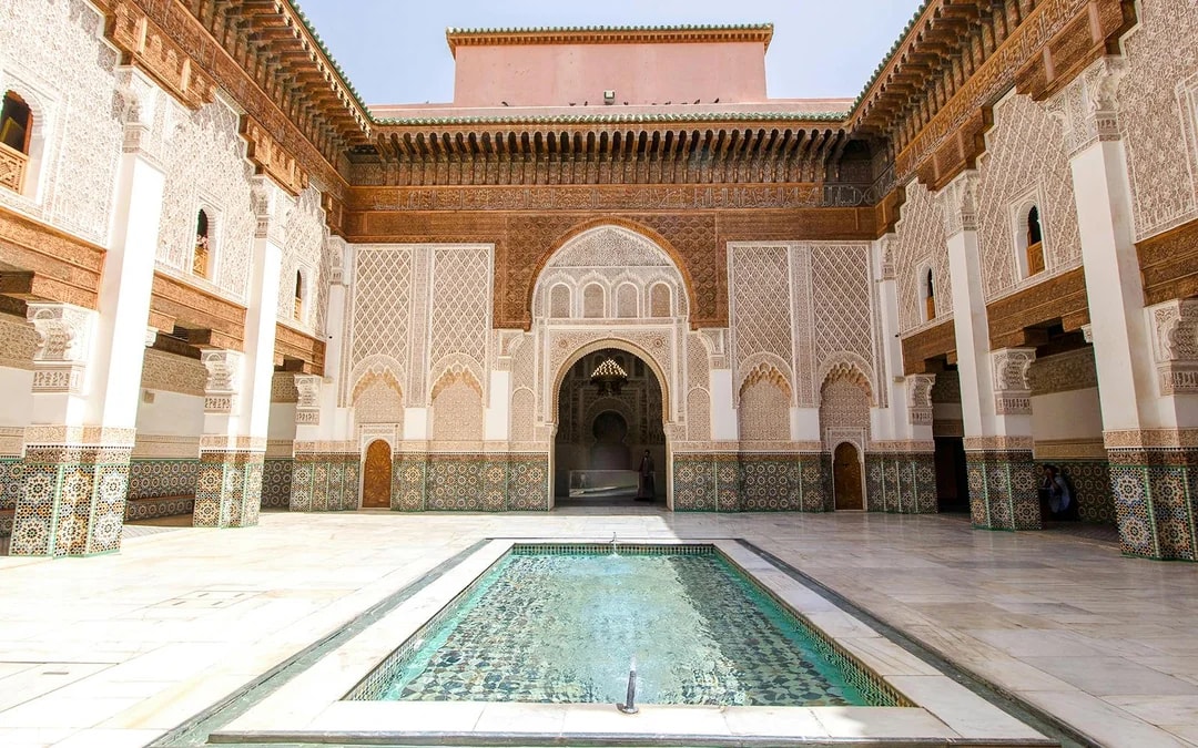 Ben Youssef Madrasa courtyard with intricate tilework and central pool in Marrakech, Morocco.
