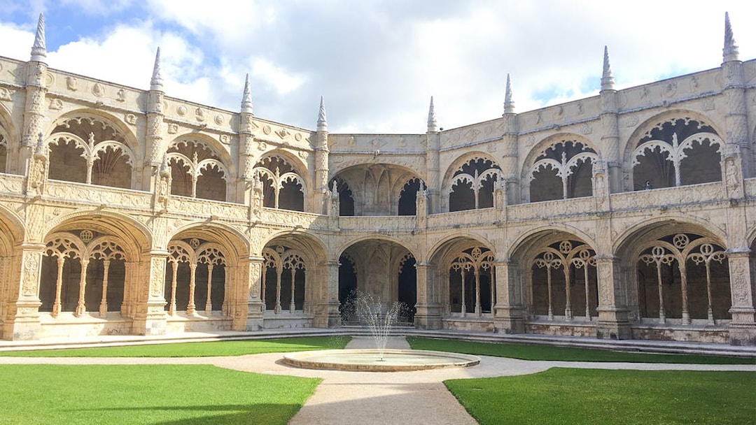 Jerónimos Monastery courtyard with ornate arches and central fountain in Lisbon, Portugal.