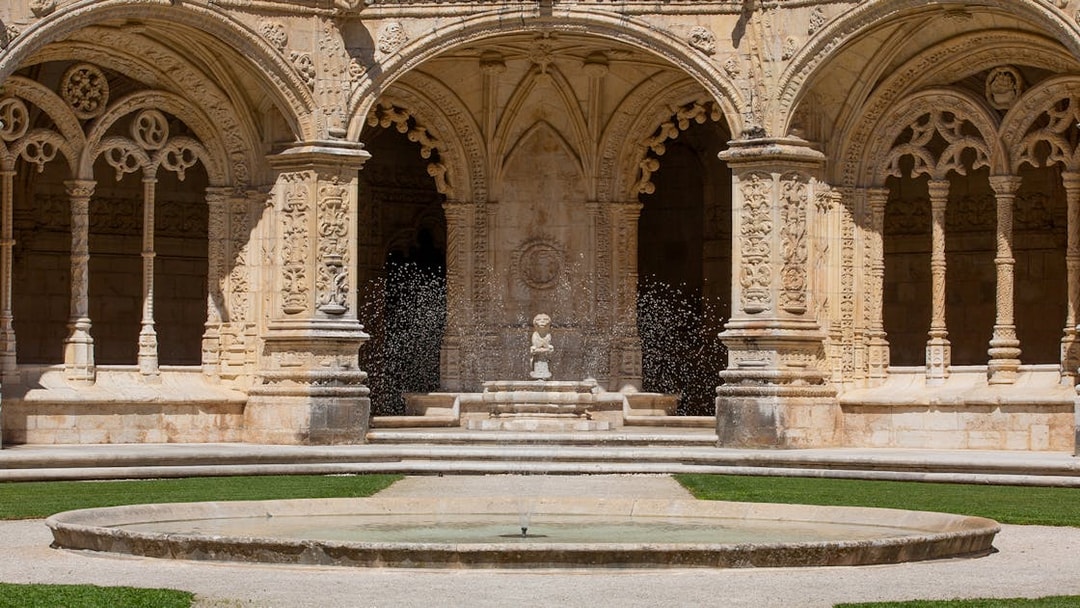 Jerónimos Monastery cloister with ornate arches and central fountain in Lisbon.