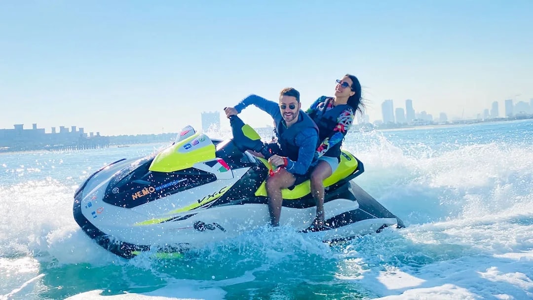 Tourists riding a jet ski in Dubai with city skyline in the background.